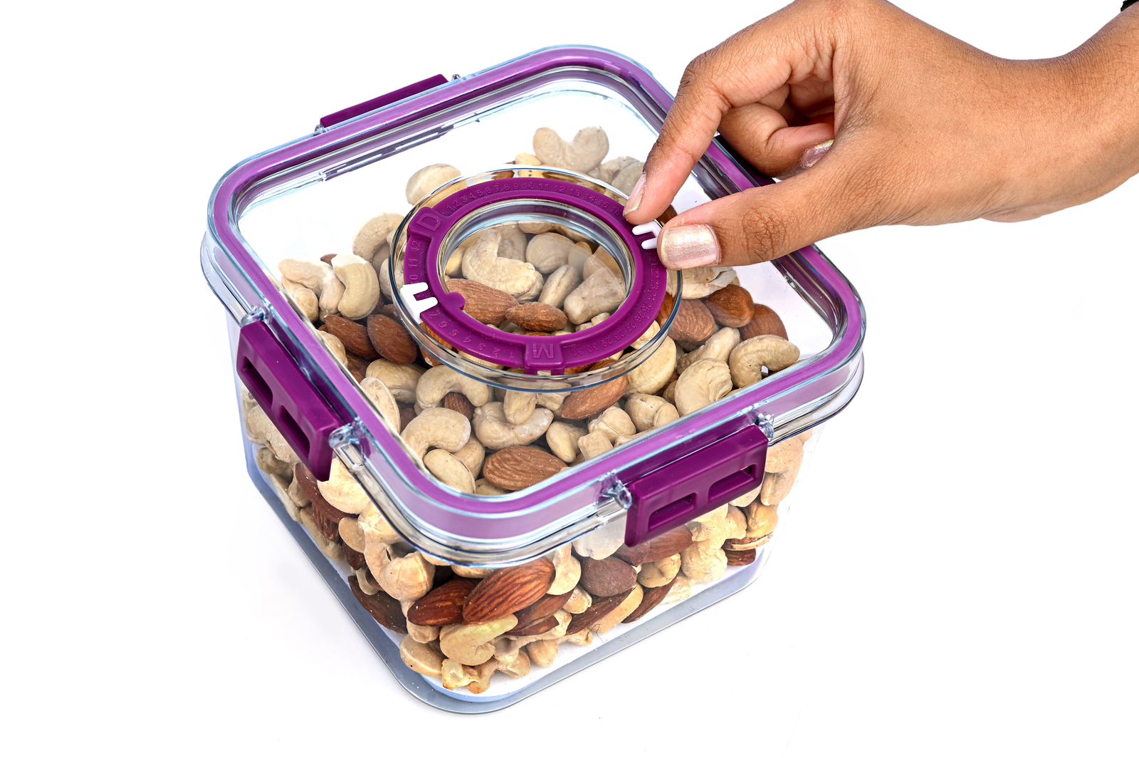 Hand opening a transparent container filled with nuts and seeds, with a purple lid.