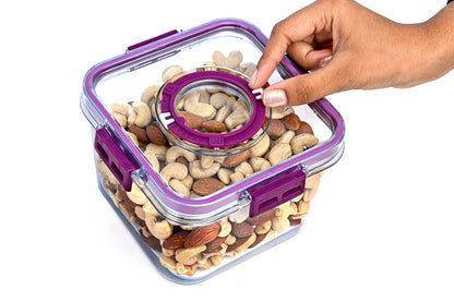 Hand opening a transparent container filled with nuts and seeds, with a purple lid.